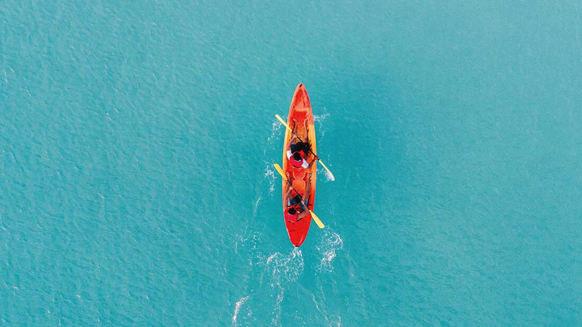 Ein Kanu mit zwei Insassen, von oben fotografiert, steuert zielstrebig durch türkisfarbenes Wasser.