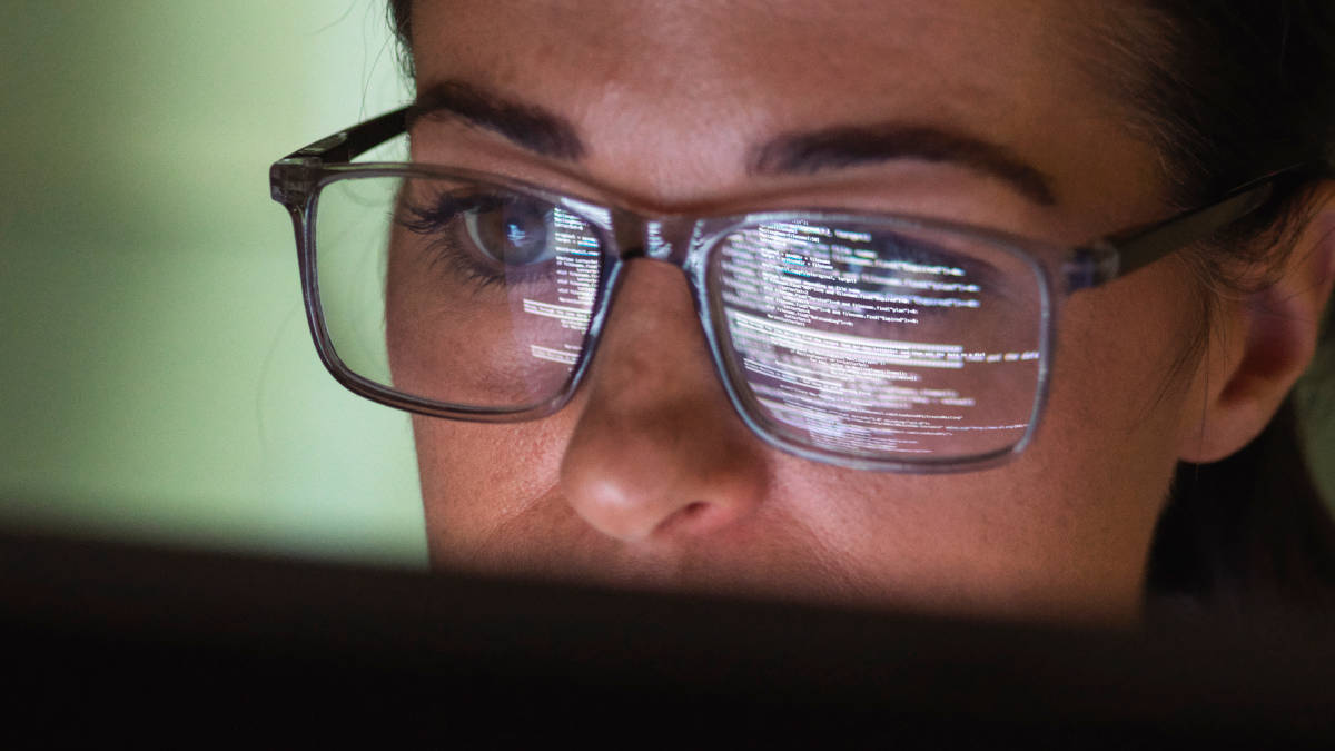 Gesicht einer Frau mit Brille, in der sich Programmcode vom Computer-Bildschirm spiegelt